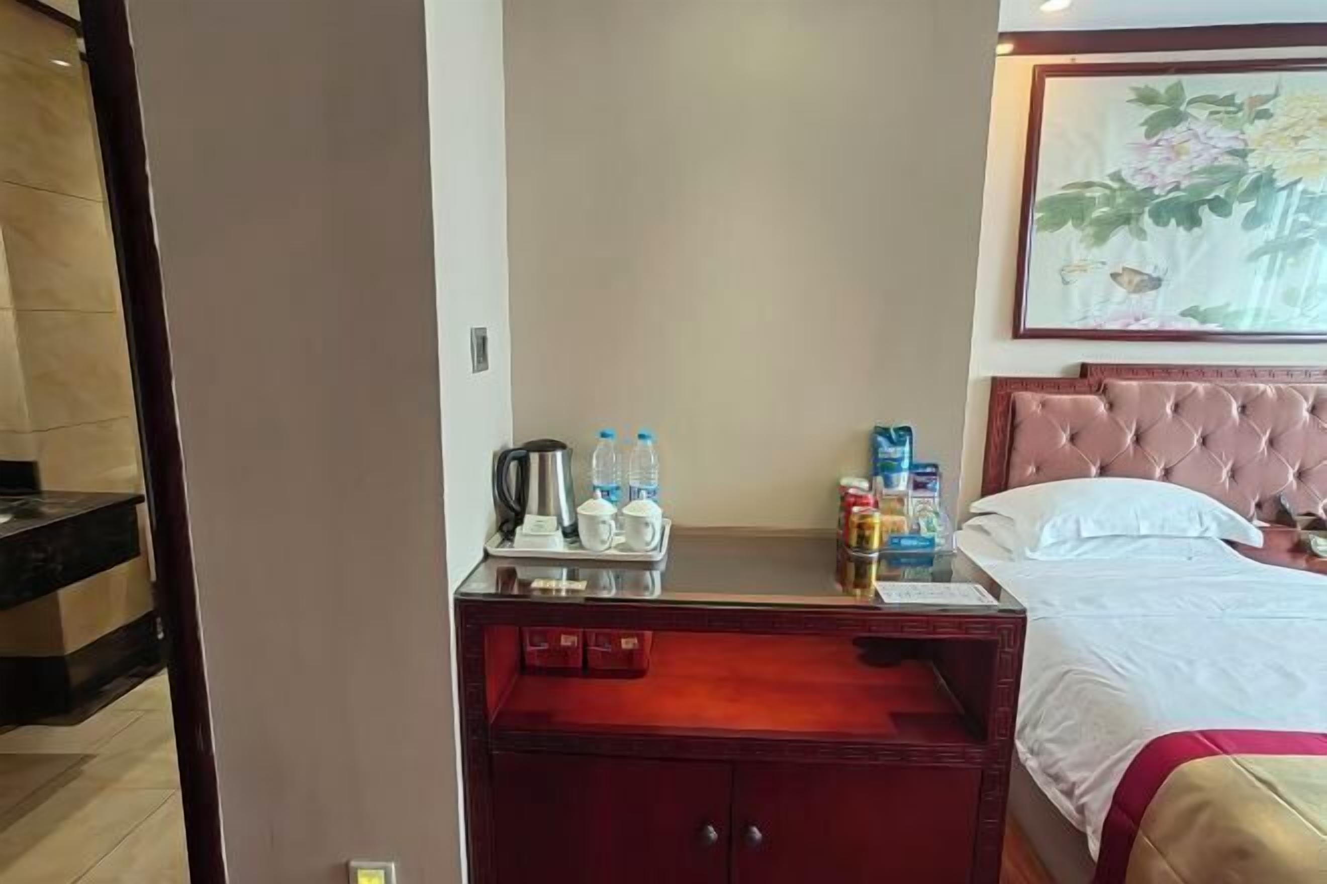 A hotel room with a bed, a bedside table with a tray of toiletries, a nightstand, and a painting on the wall.