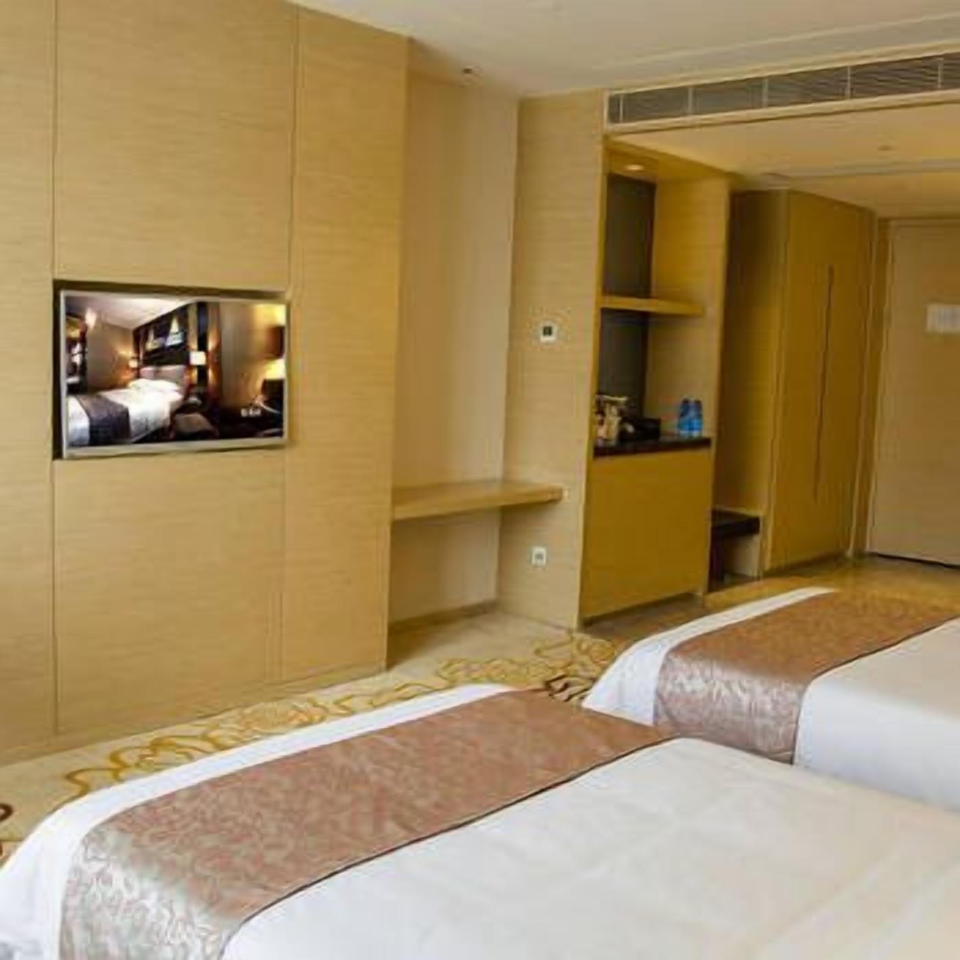 A hotel room with two beds, a TV mounted on the wall, and a small seating area.