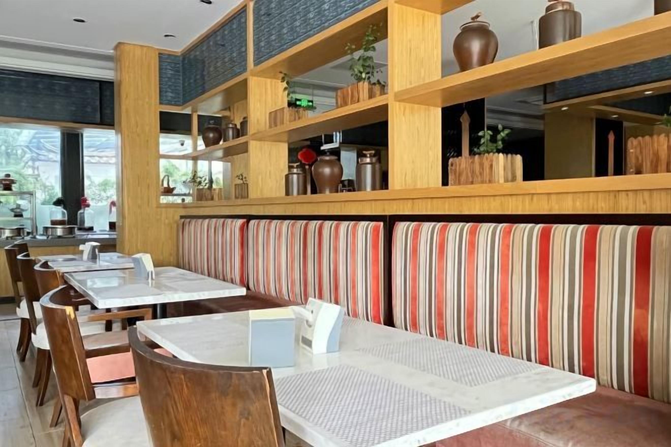 Un restaurante con estantes de madera altos, asientos con cojines a rayas y mesas con manteles individuales blancos.