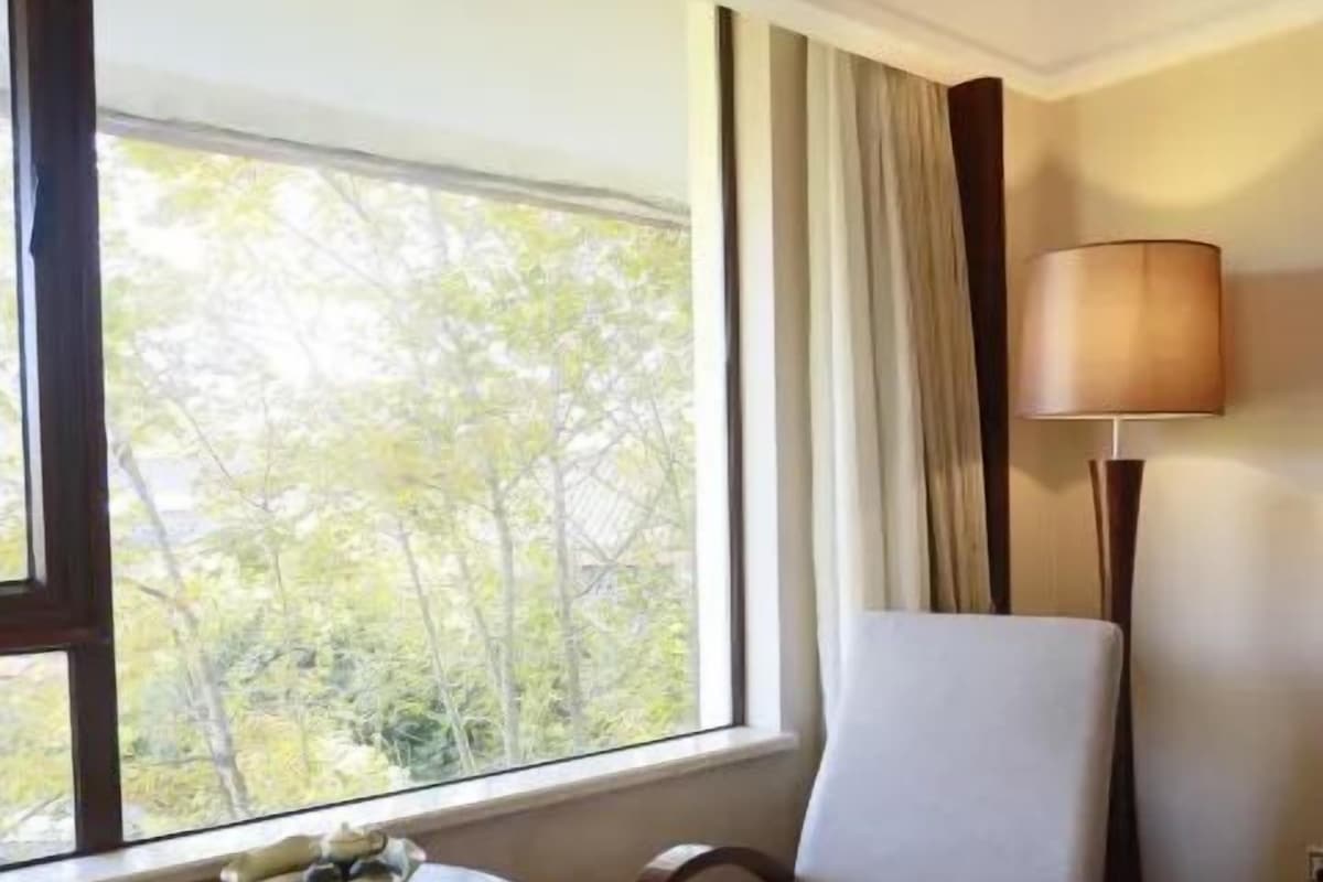 A hotel room with a window, a chair, a small table with a bowl, and a lamp.
