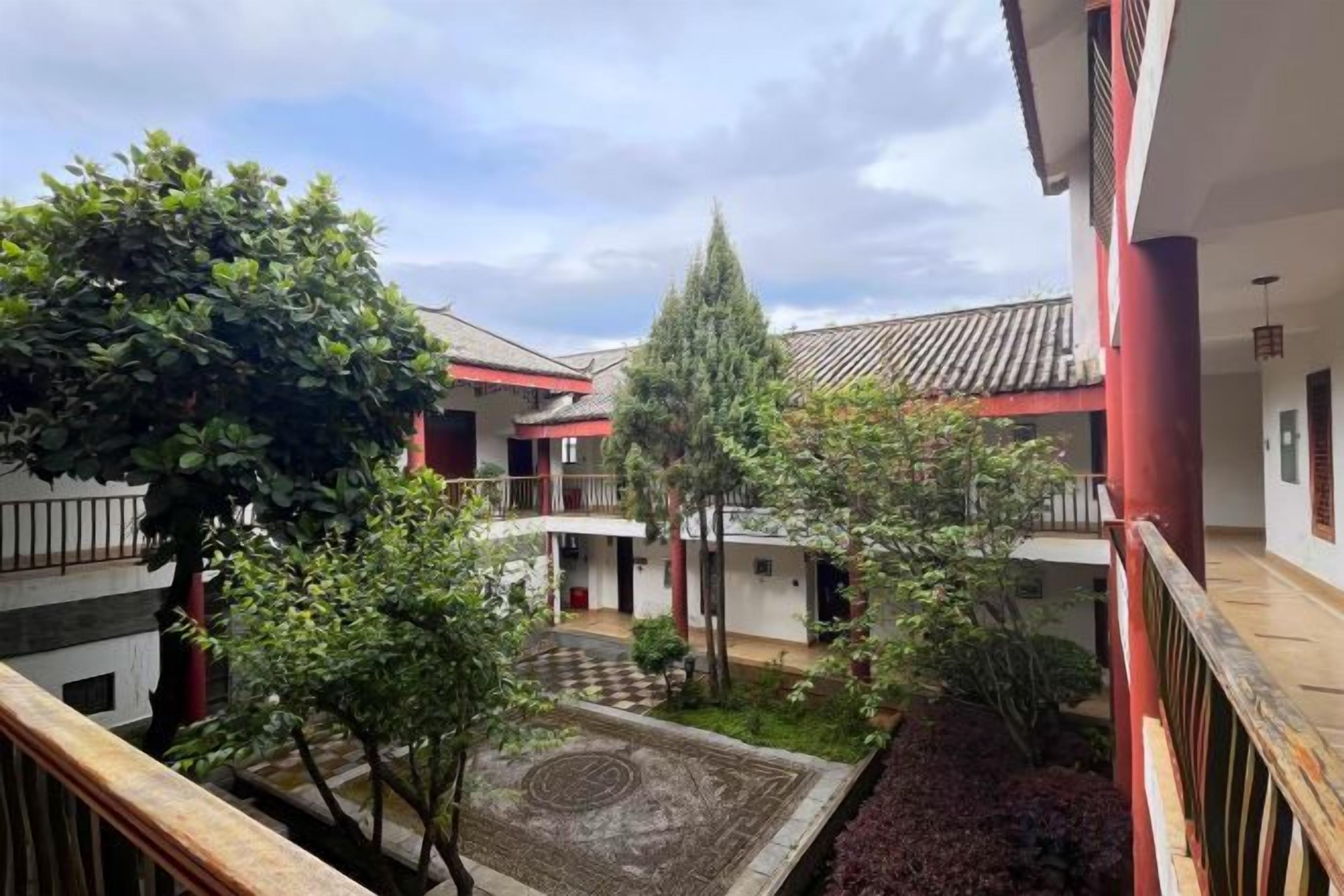 A courtyard with a central circular pattern, surrounded by trees and buildings with red accents.