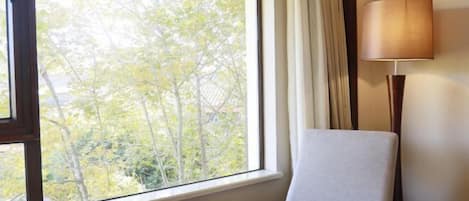 A room with a large window, a chair, a table with a bowl, and a lamp.