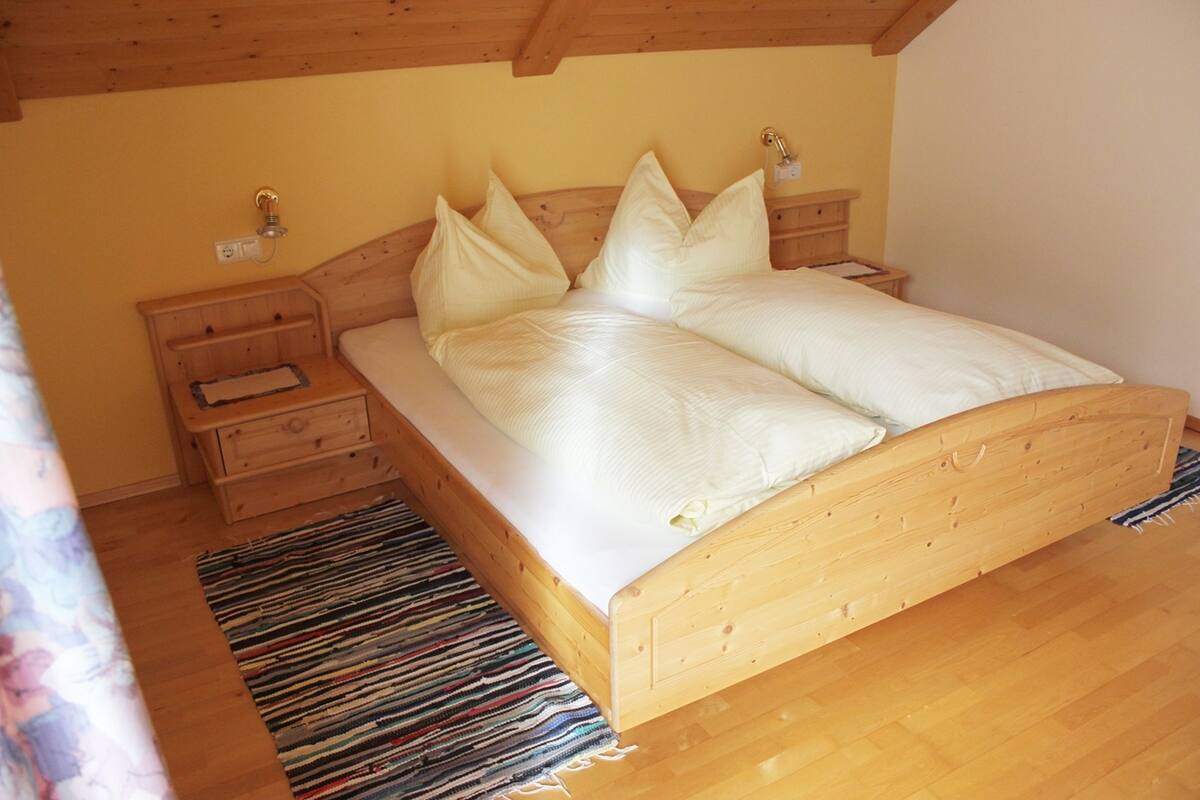 Ein hölzernes Bett mit weißer Bettwäsche in einem Raum mit Holzböden und -wänden.