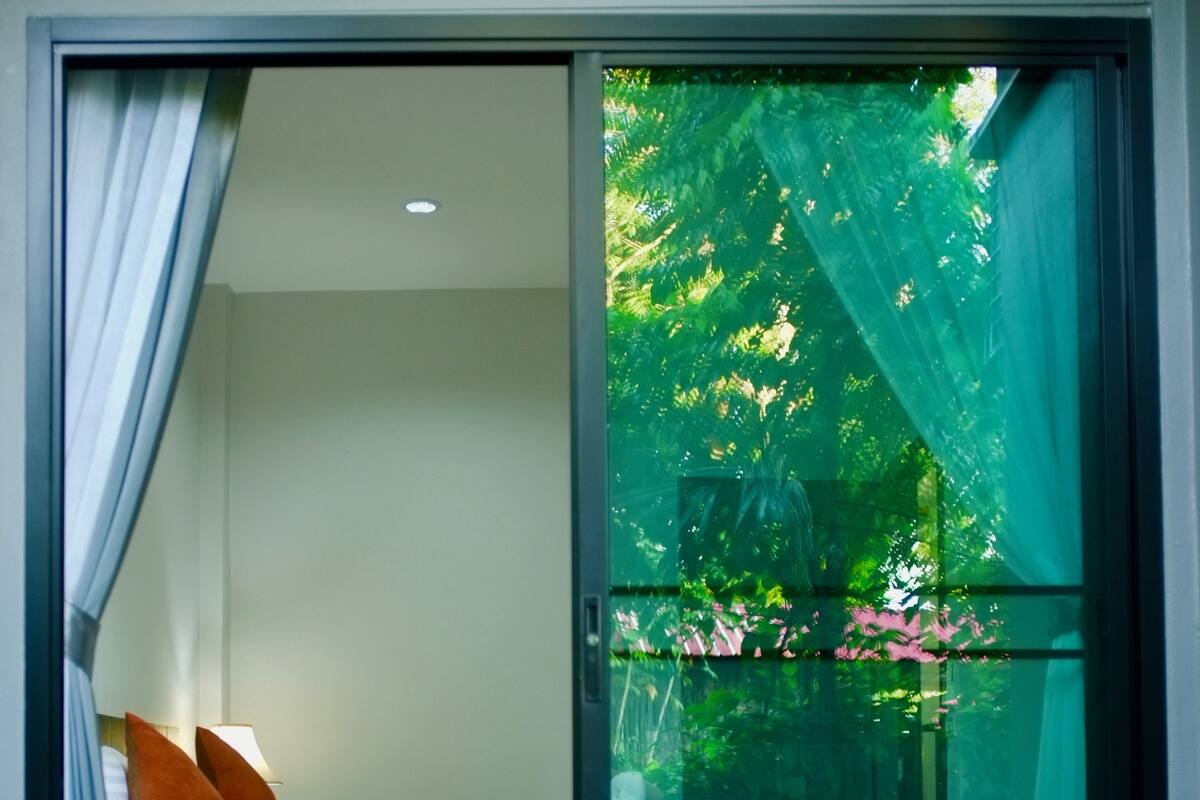 Quarto com porta de vidro deslizante para uma varanda, uma cadeira de madeira e uma pequena mesa com uma planta.