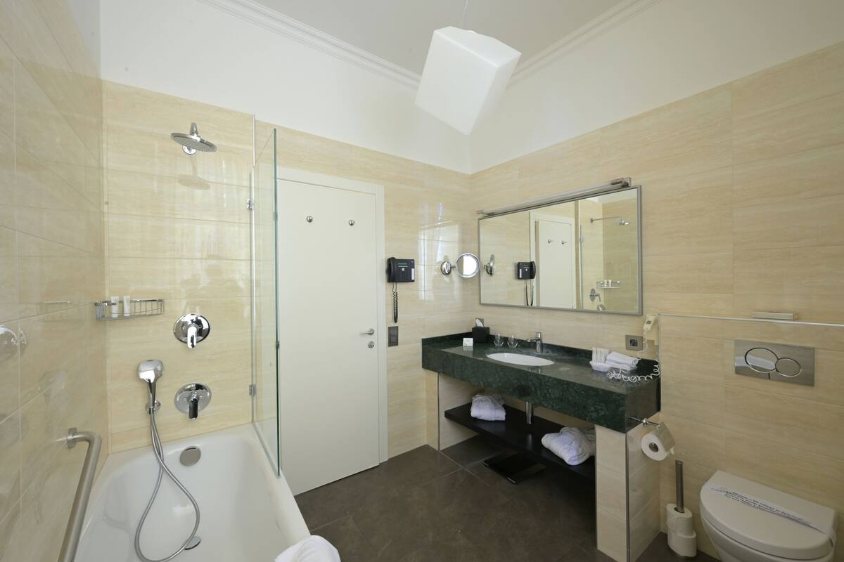 Un baño moderno con ducha de vidrio, lavabo con encimera de mármol, espejo grande y un inodoro.