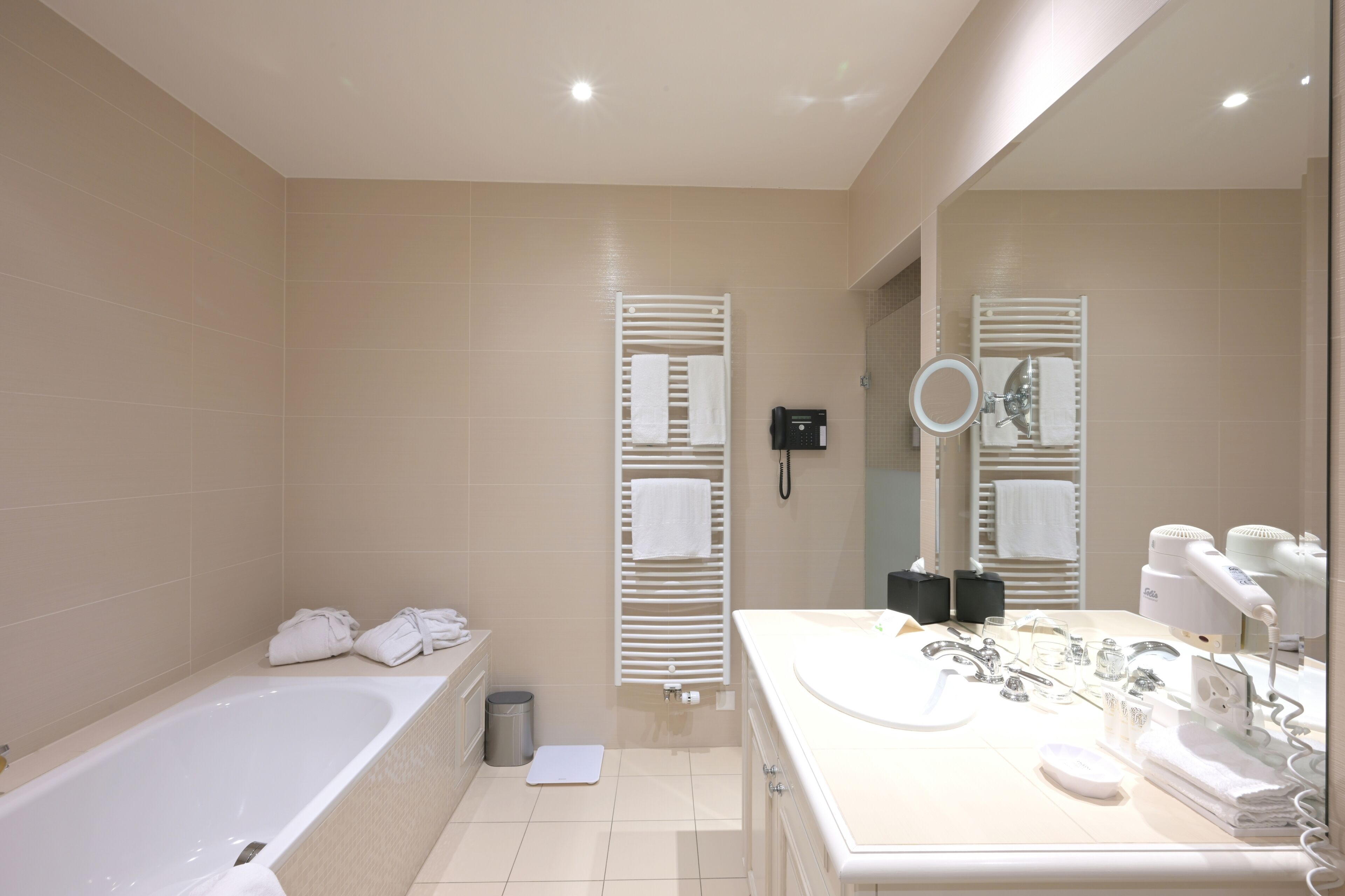 A modern bathroom with a bathtub, a large mirror, and a vanity with a sink and hairdryer.