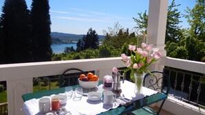 A table set on a balcony with a view of a lake and mountains, a vase of pink flowers, and a bowl of oranges. - White Lilac romantic B&B adults only (Arona)