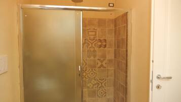 Box doccia in vetro con piastrelle decorate e porta bianca.