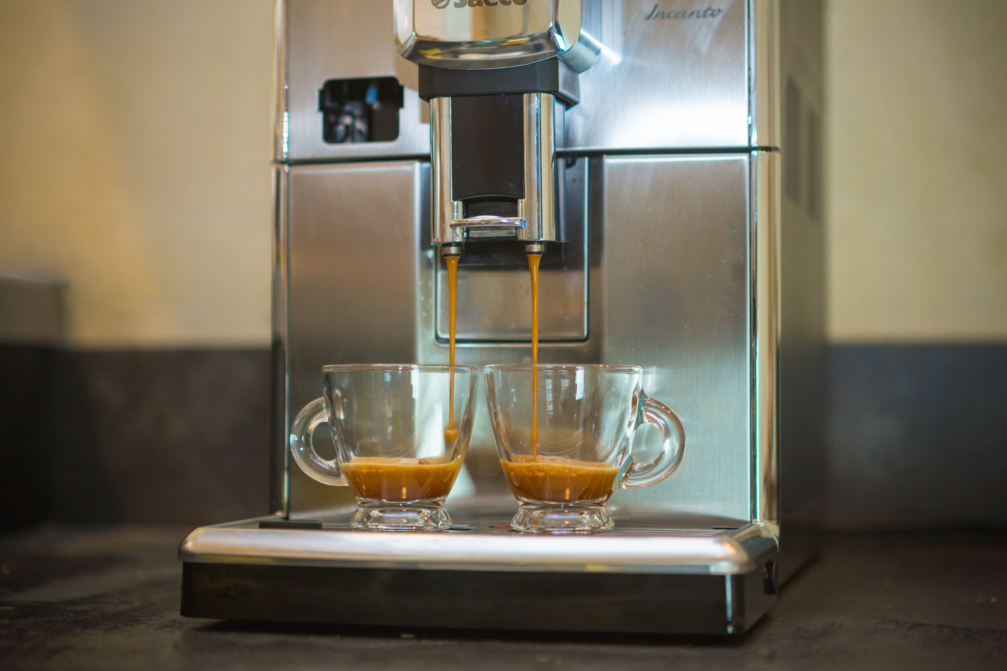 Une machine à café verse de l’expresso dans deux tasses en verre transparent.
