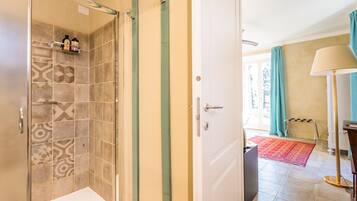 Une salle de bain avec des carreaux décorés, une douche et une porte donnant sur une pièce où se trouvent un tapis et une lampe.