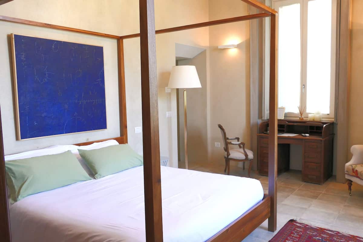 Un dormitorio con cama con dosel, un escritorio con silla, un televisor y una obra de arte azul grande en la pared.