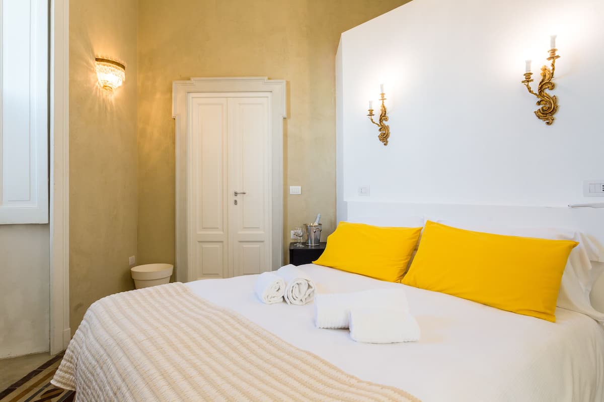 Una habitación de hotel con una cama, una puerta blanca y una mesita de noche con una lámpara.