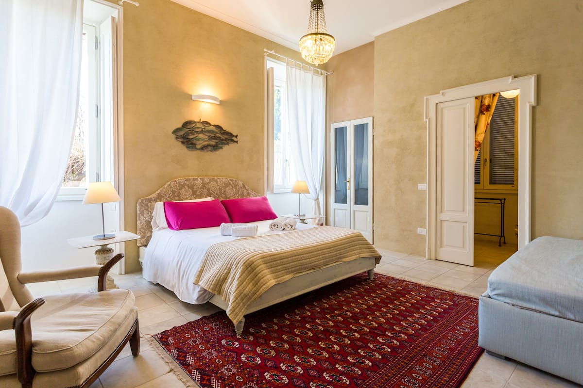 Un dormitorio con cama, una silla, una mesa y un tapete rojo estampado.