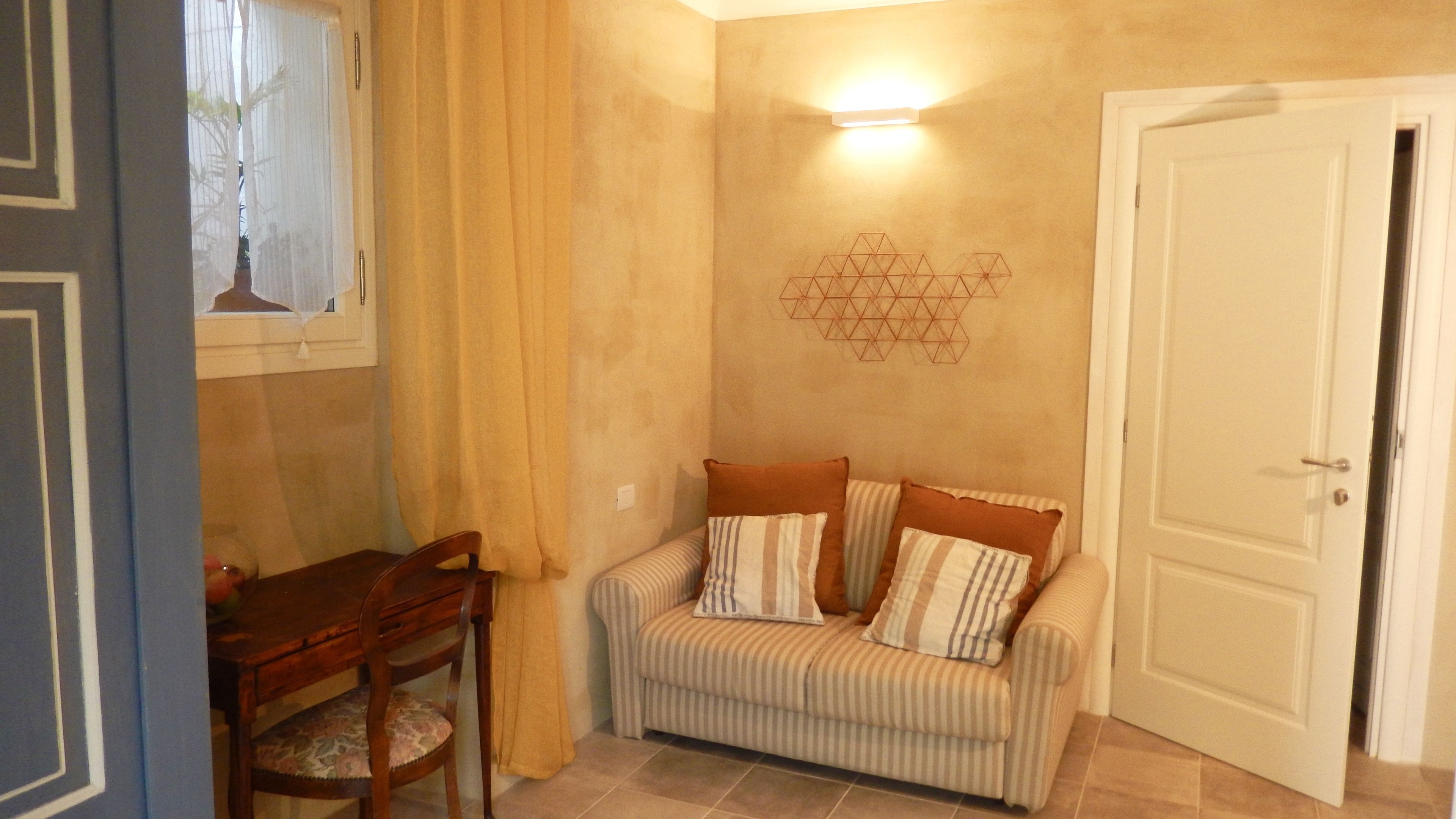 A room with a striped sofa, a wooden chair, a table, and a geometric wall decoration.