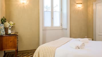 Una habitación de hotel con una cama, una mesita de noche de madera, una ventana y dos apliques de pared.