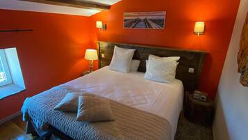 Een slaapkamer met een groot bed, houten balken, een raam en een schilderij aan de muur.
