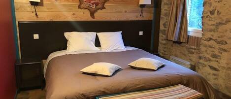 A bedroom with a wooden headboard, two bedside lamps, a bed with two pillows, a striped bench, and a window with curtains.