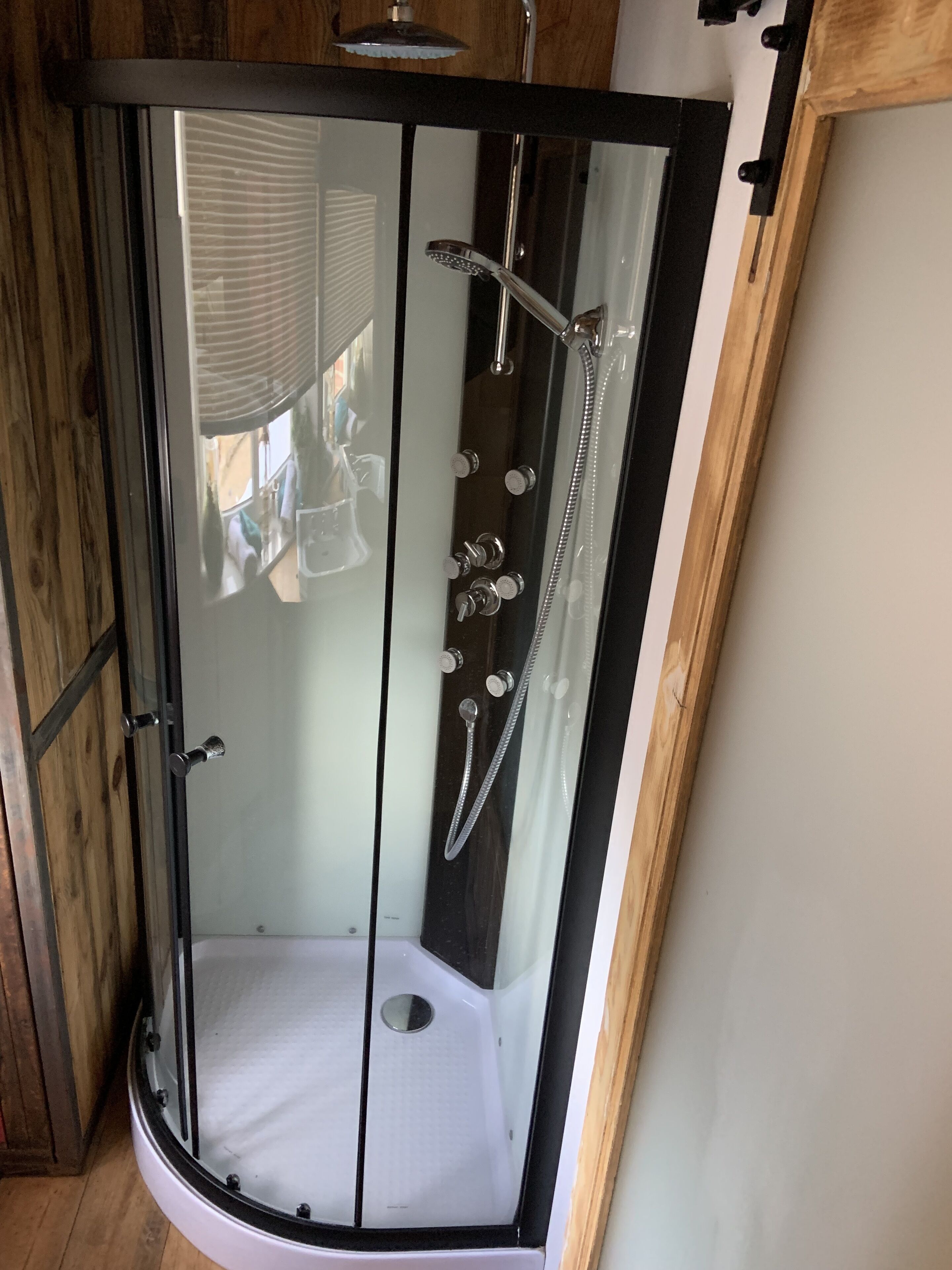 A glass-enclosed shower with a white floor, a handheld showerhead, and a wall-mounted faucet.