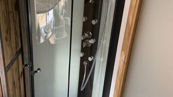A glass-enclosed shower with a white floor, a handheld showerhead, and a wall-mounted faucet.