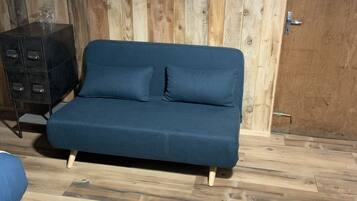A room with a blue sofa, wooden flooring, a metal cabinet, and a wooden wall.
