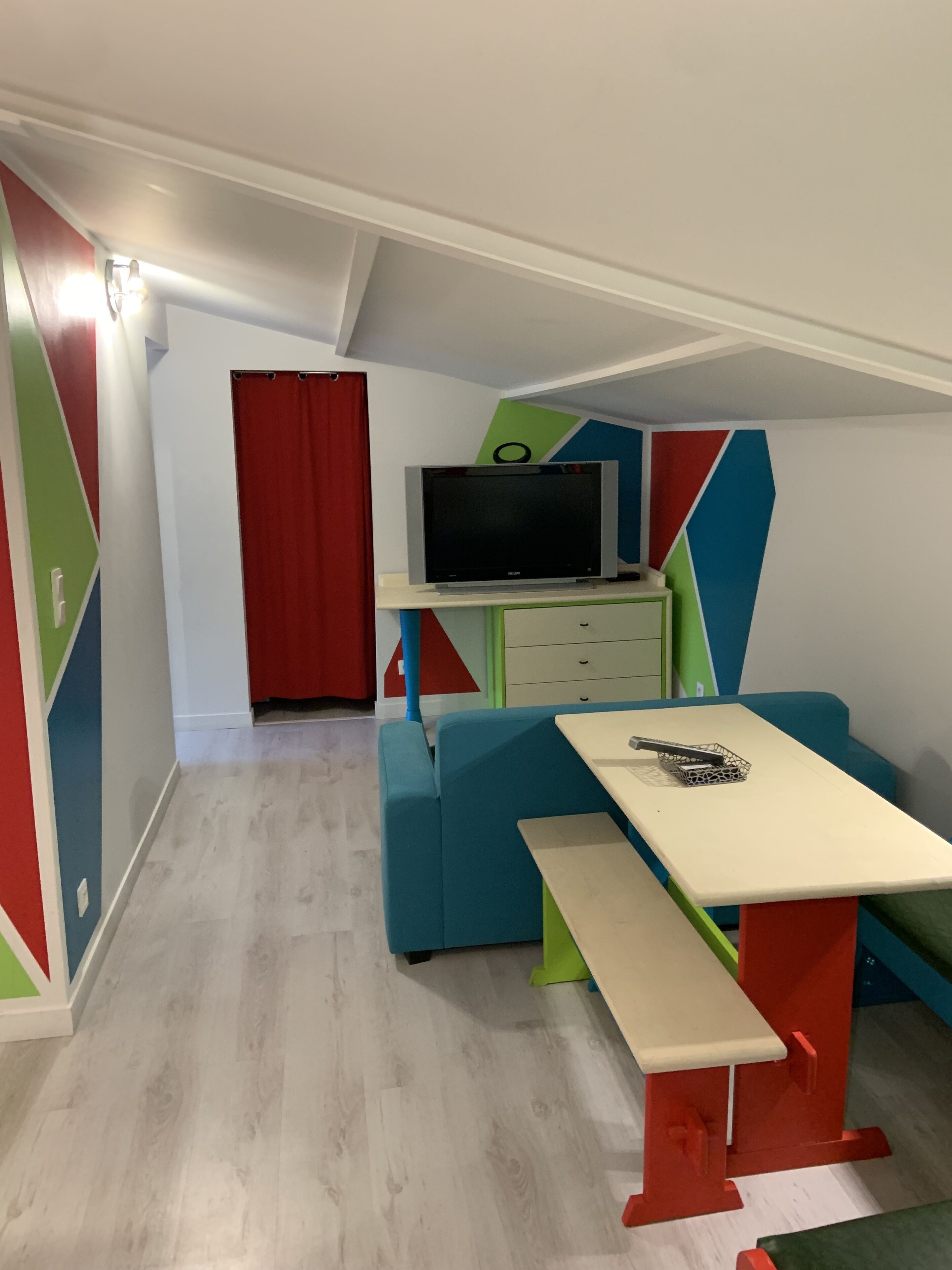 Una habitación con sofá, una mesa, televisor sobre un mueble y una puerta roja.