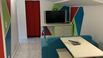 Una habitación con sofá, una mesa, televisor sobre un mueble y una puerta roja.