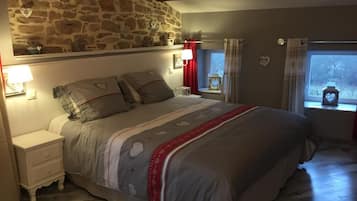 A bedroom with a stone wall, a bed with a patterned bedspread, bedside lamps, and a window with curtains.