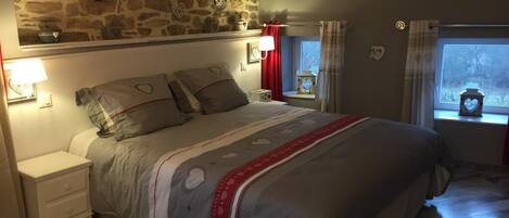 Un dormitorio con pared de piedra, una cama con cubrecama estampado, lámparas de noche y una ventana con cortinas.