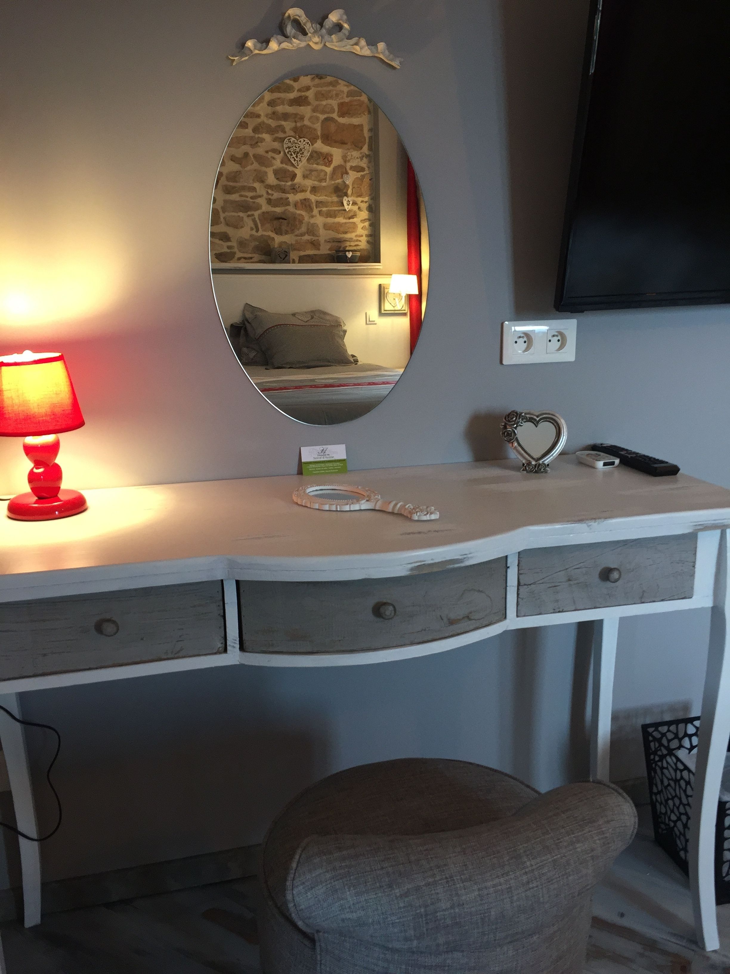 A white vanity with a mirror, a red lamp, a heart-shaped decoration, and a small table with a remote control.