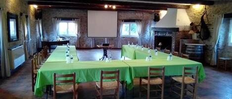 Una larga mesa de comedor con manteles verdes y sillas, ubicada en una habitación rústica con paredes de piedra y una chimenea.