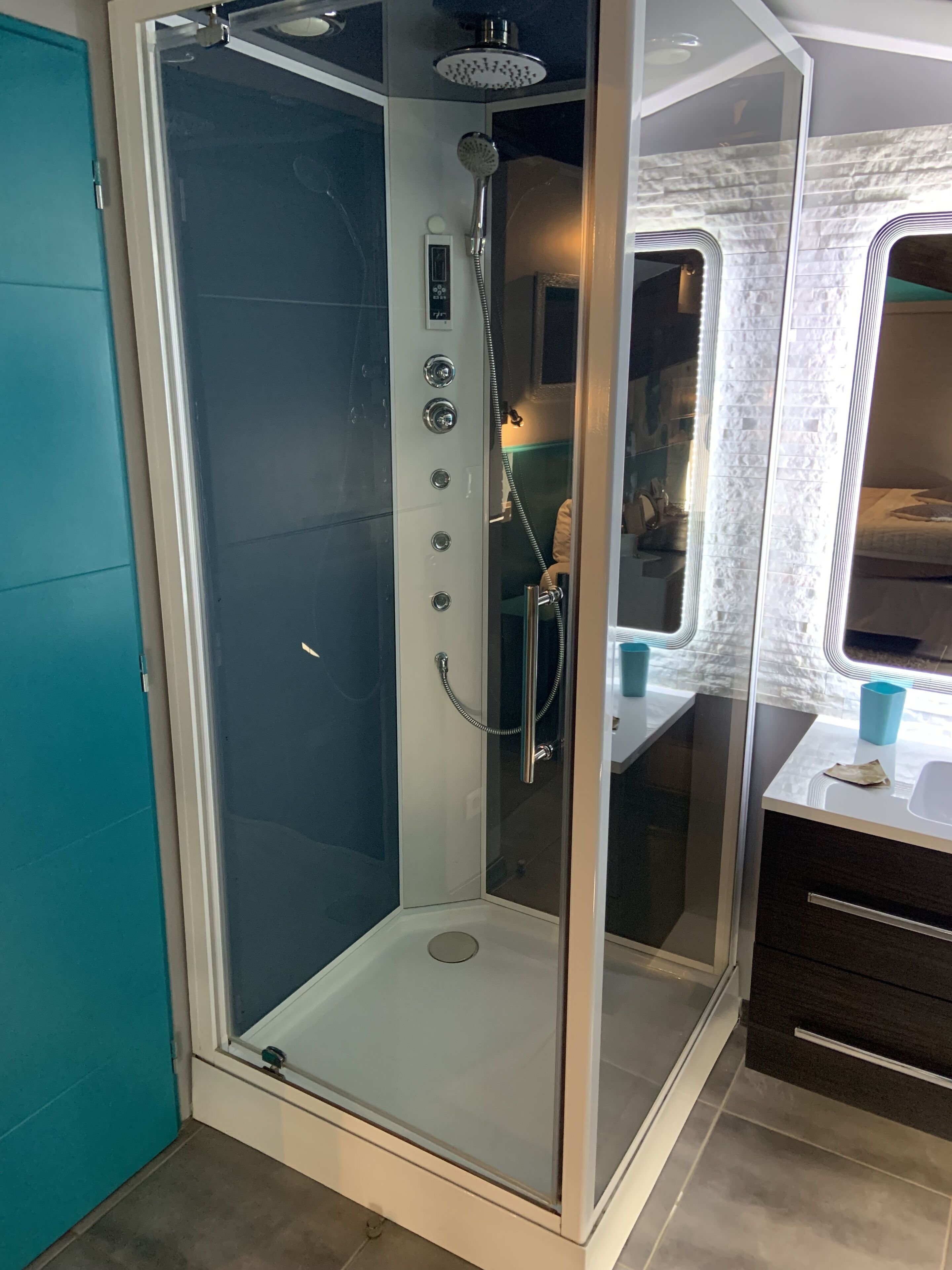 A glass-enclosed shower with a handheld showerhead and control panel.