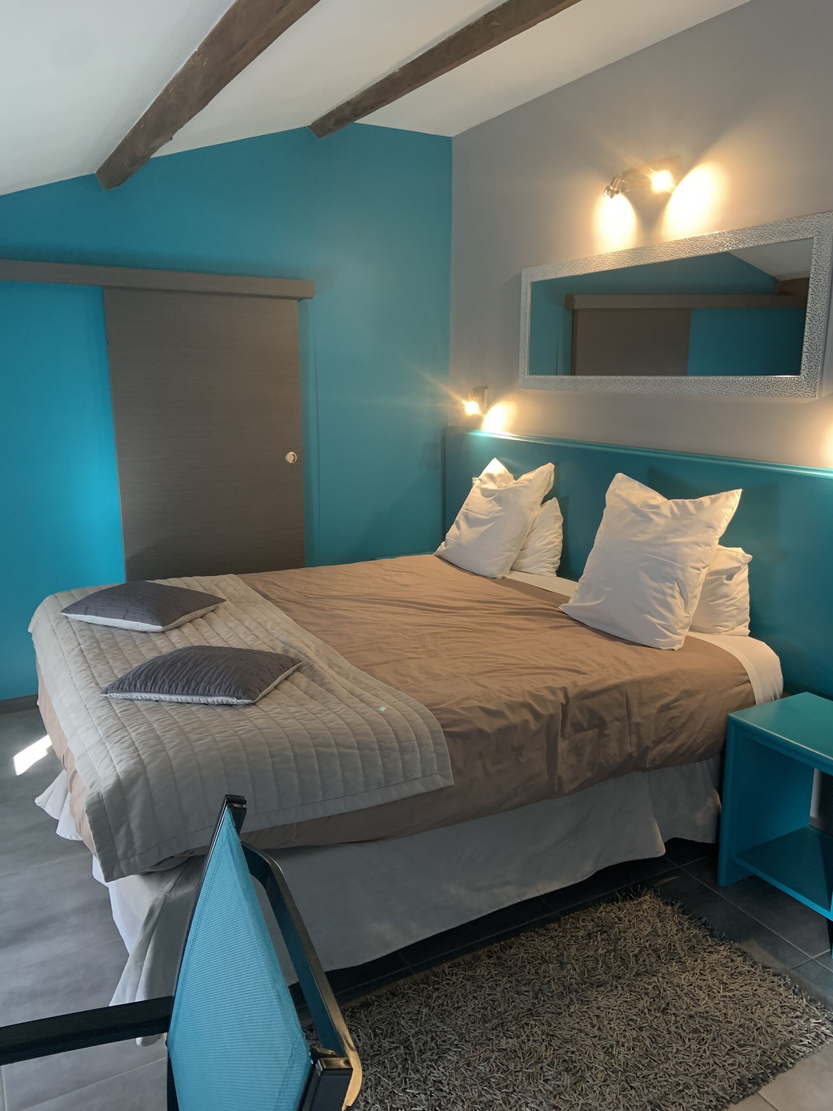 A bedroom with a bed, pillows, a nightstand, a mirror, and a window.