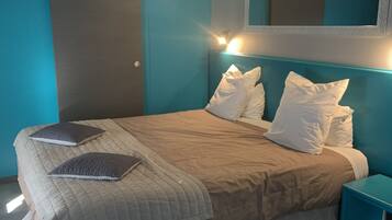 A bedroom with a bed, pillows, a nightstand, a mirror, and a window.