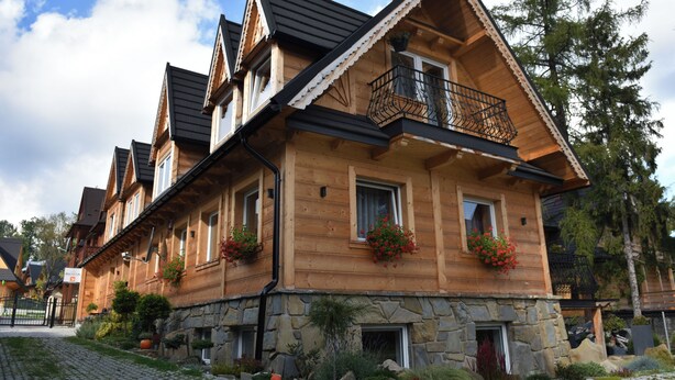 Un chalet en bois, doté de fondations en pierre, de plusieurs balcons et de jardinières fleuries.