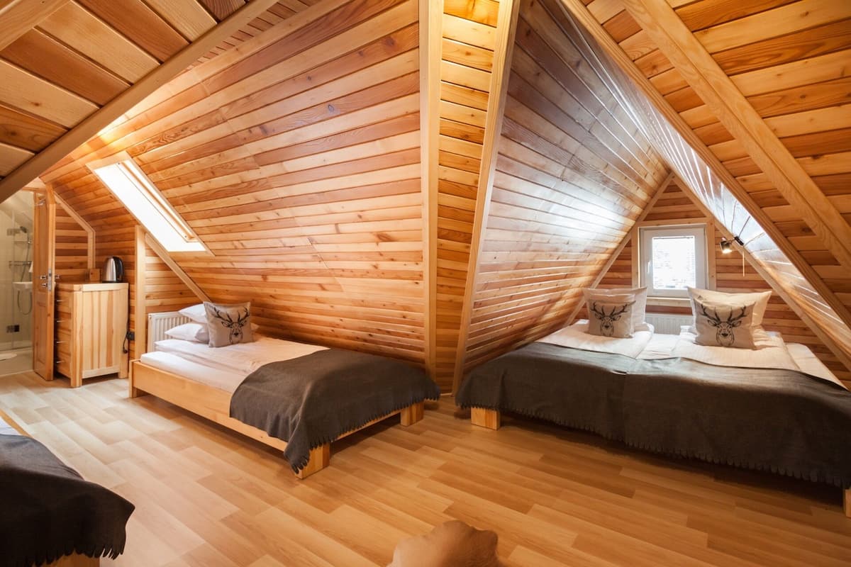 Een gezellige slaapkamer op zolder met houten wanden en schuine plafonds, met twee bedden met bijpassende kussens en een klein raam.