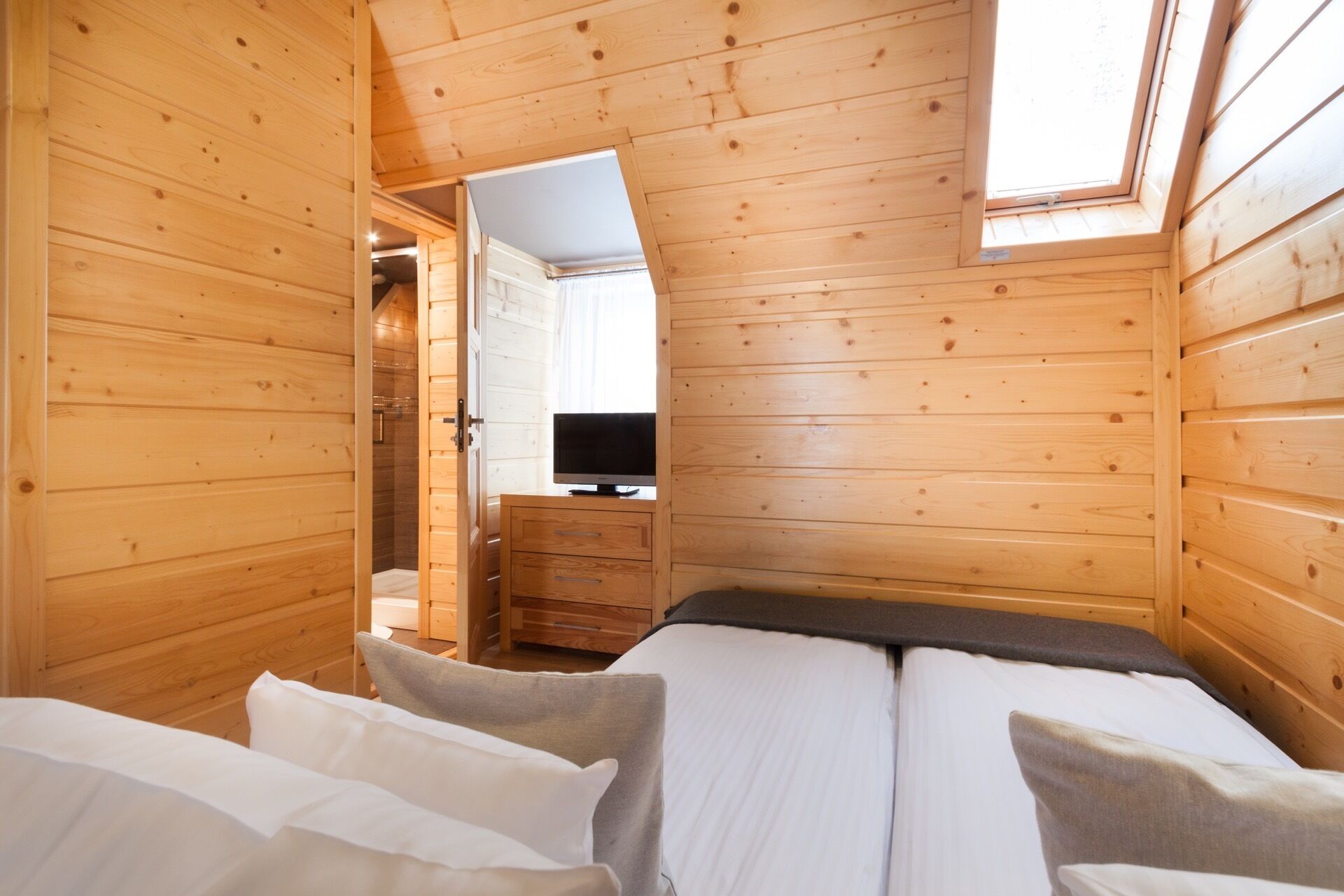 A wooden cabin room with a bed, a television, and a shower area.