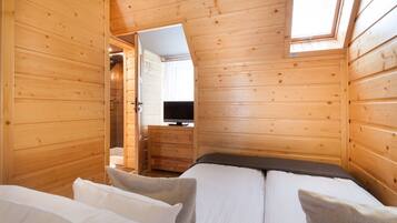 A wooden cabin room with a bed, a television, and a shower area.