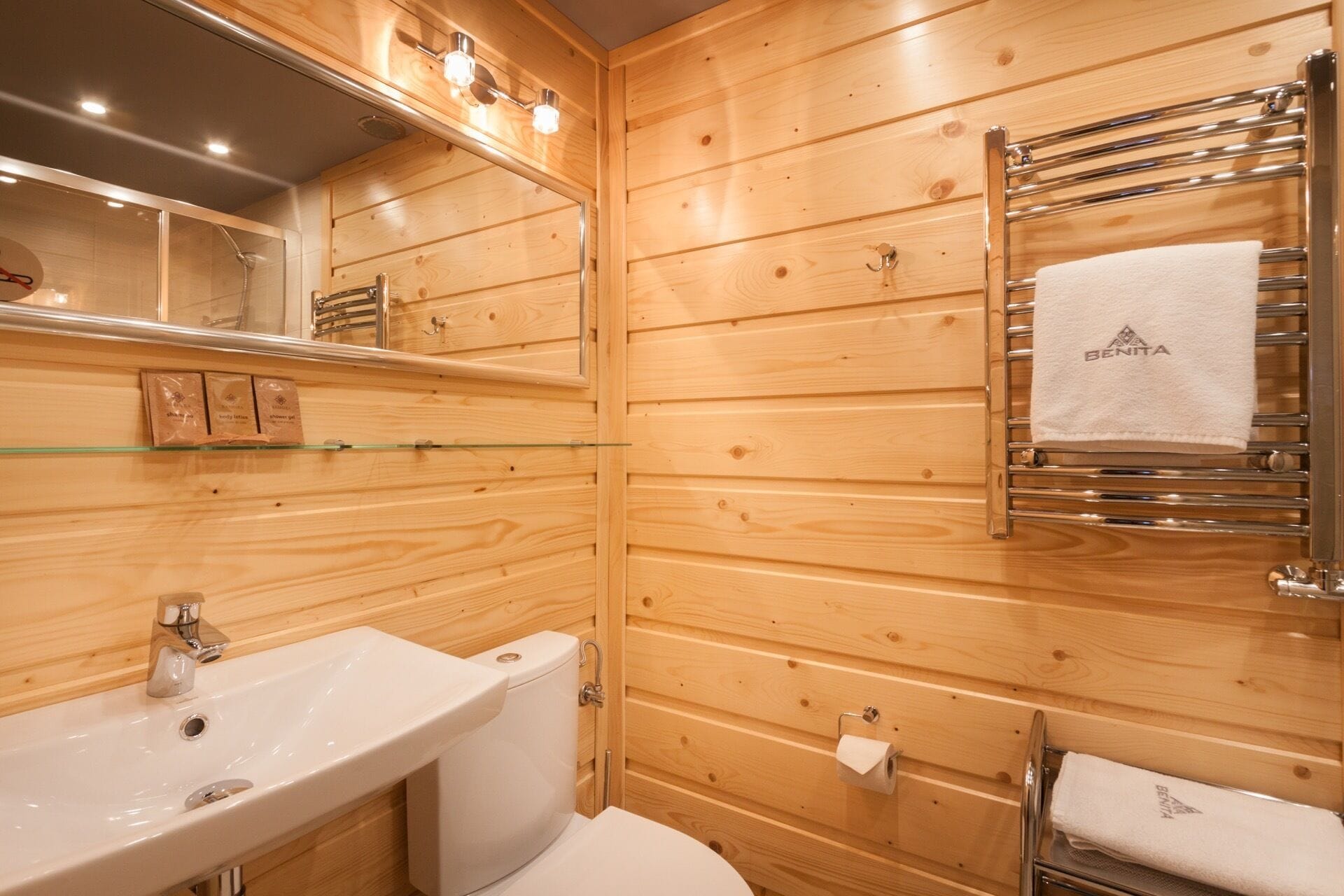Un baño con paneles de madera, estante de vidrio, lavamanos, inodoro y toallero con una toalla.