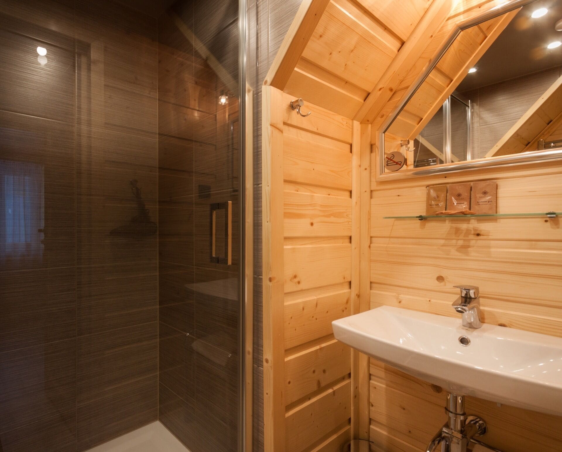 A wooden cabin bathroom with a glass shower enclosure, a white sink, and a wooden ceiling with a skylight.
