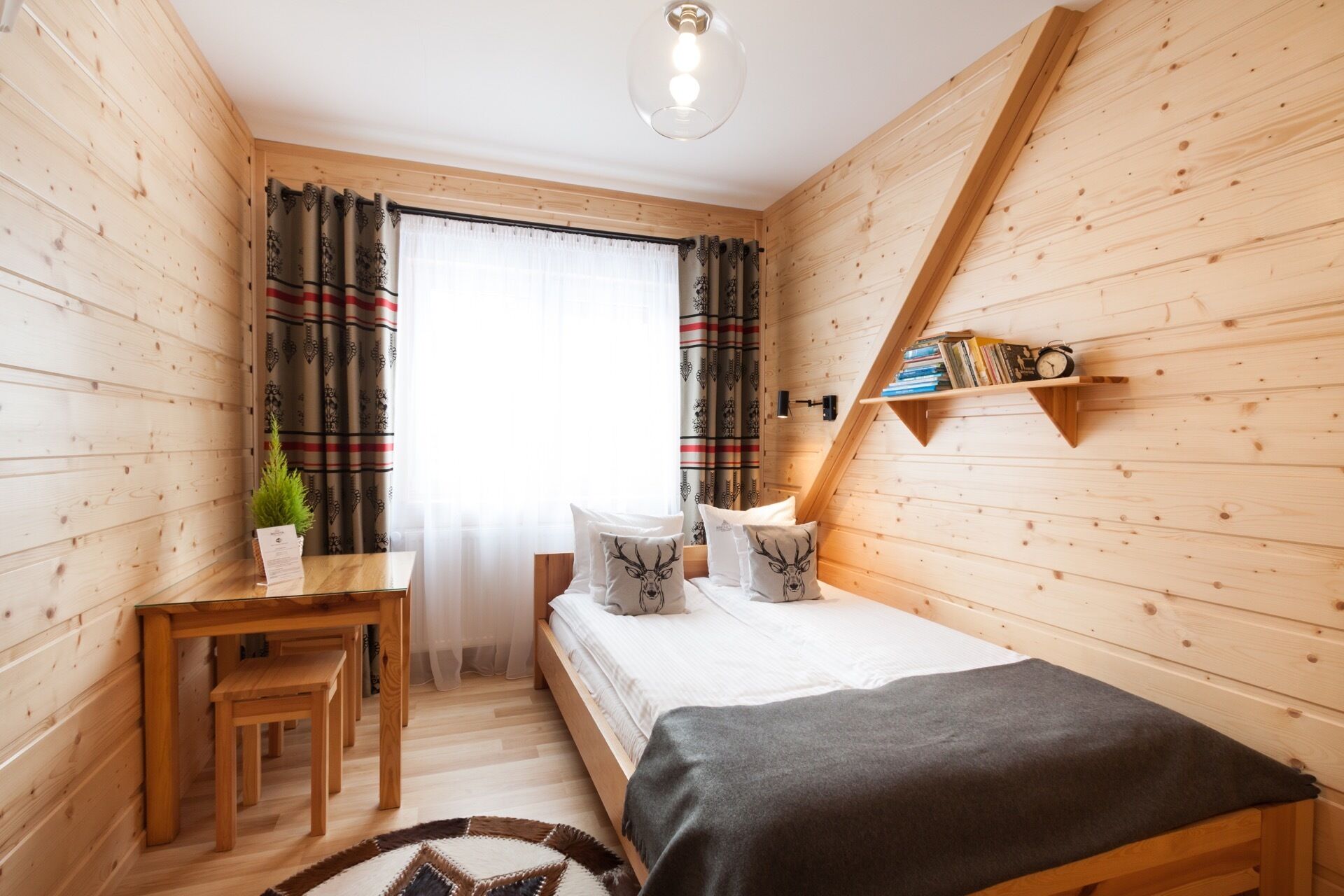 A cozy wooden room with a bed, a desk, and a shelf with books and a clock.