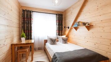 A cozy wooden room with a bed, a desk, and a shelf with books and a clock.