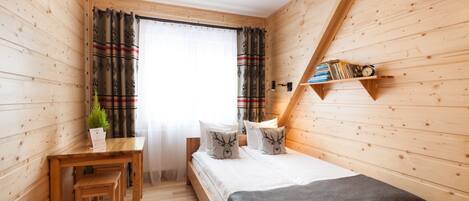 A cozy wooden room with a bed, a desk, and a shelf with books and a clock.