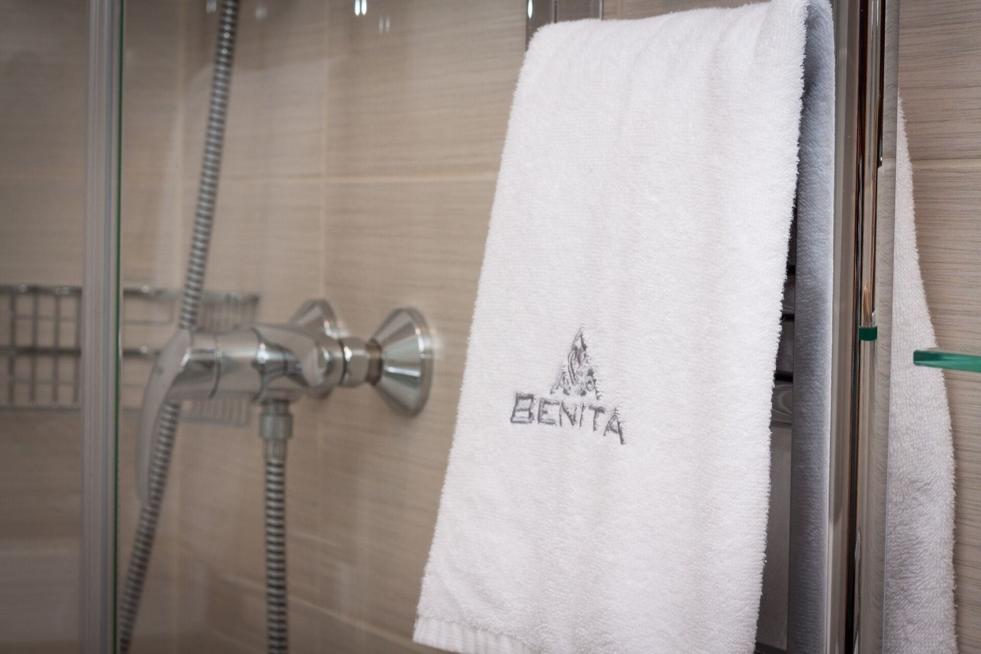 A bathroom with a glass shower enclosure, a towel hanging on the wall, and a visible showerhead.