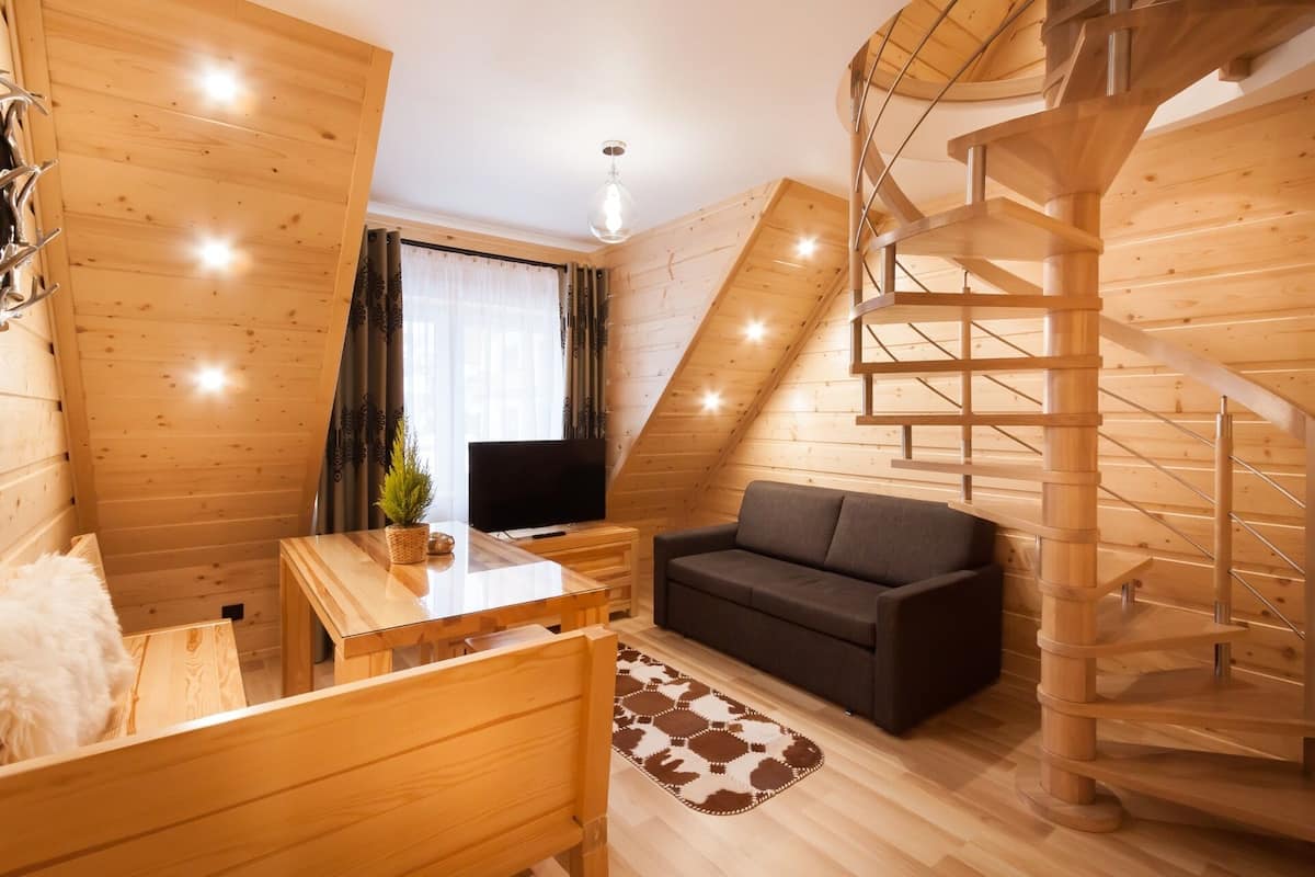 Een gezellige kamer met houten inrichting, een bank, een televisie, een eettafel en een wenteltrap.