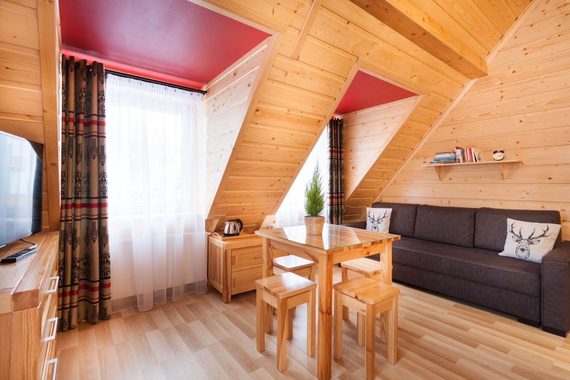 A cozy loft-style room with a wooden ceiling, a sofa, a dining table with chairs, and a TV.