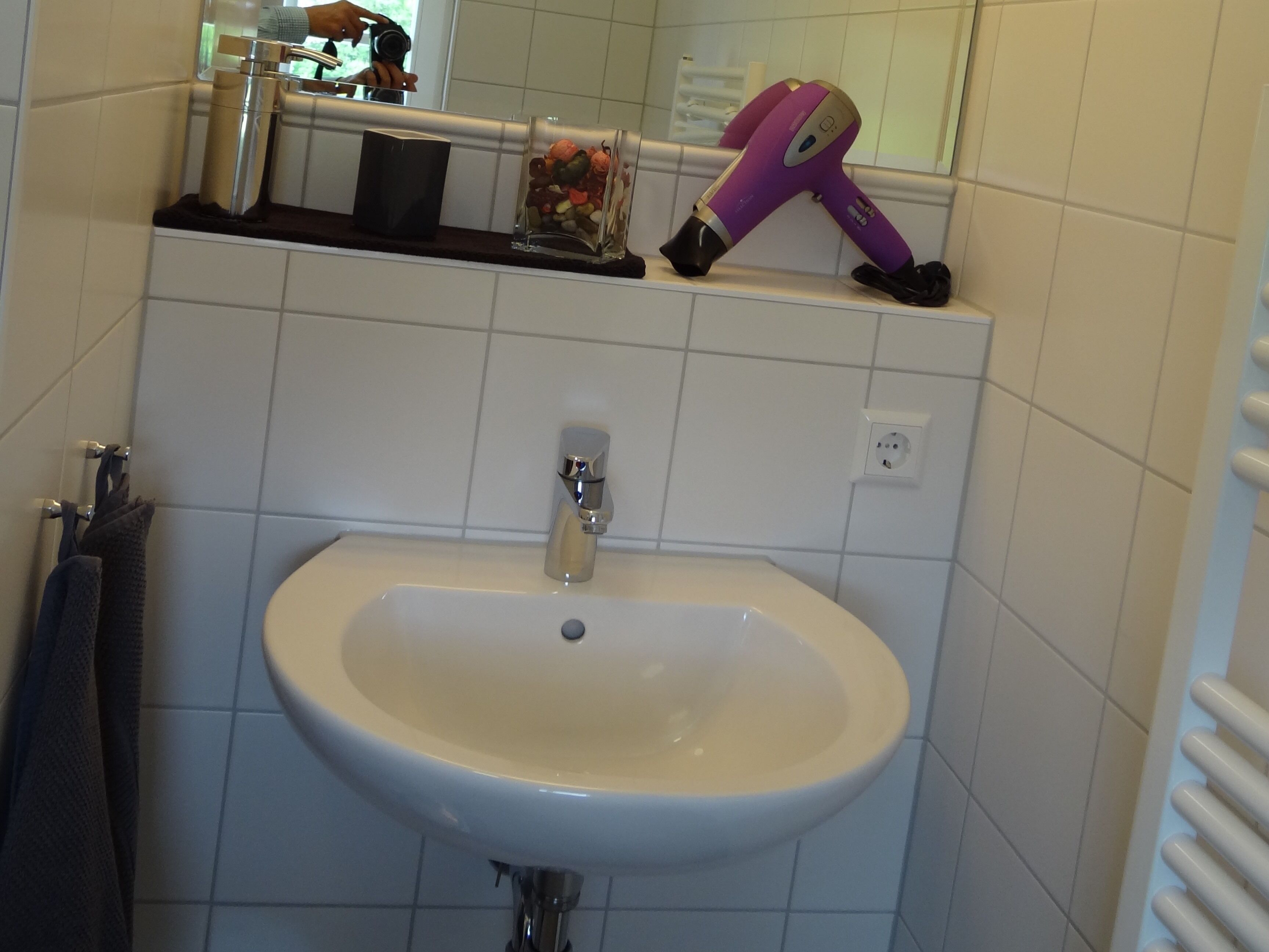 Un baño con un lavamanos blanco, un espejo y un secador de pelo sobre el mostrador.