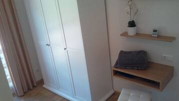 A room with a wardrobe, a TV mounted on the wall, a small shelf with a plant, and a bench.