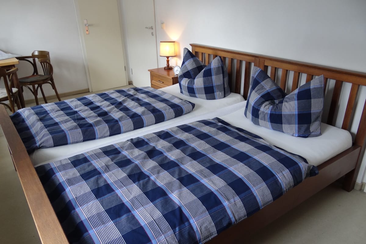 A double bed with blue and white checkered bedding, a wooden headboard, and a bedside table with a lamp.