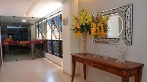 A hotel lobby with a wooden console table, a mirror with a decorative frame, and a vase of flowers. - Lis Hotel (Teresina)