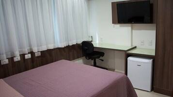 A hotel room with a bed, a desk, a chair, a television, and a small refrigerator.